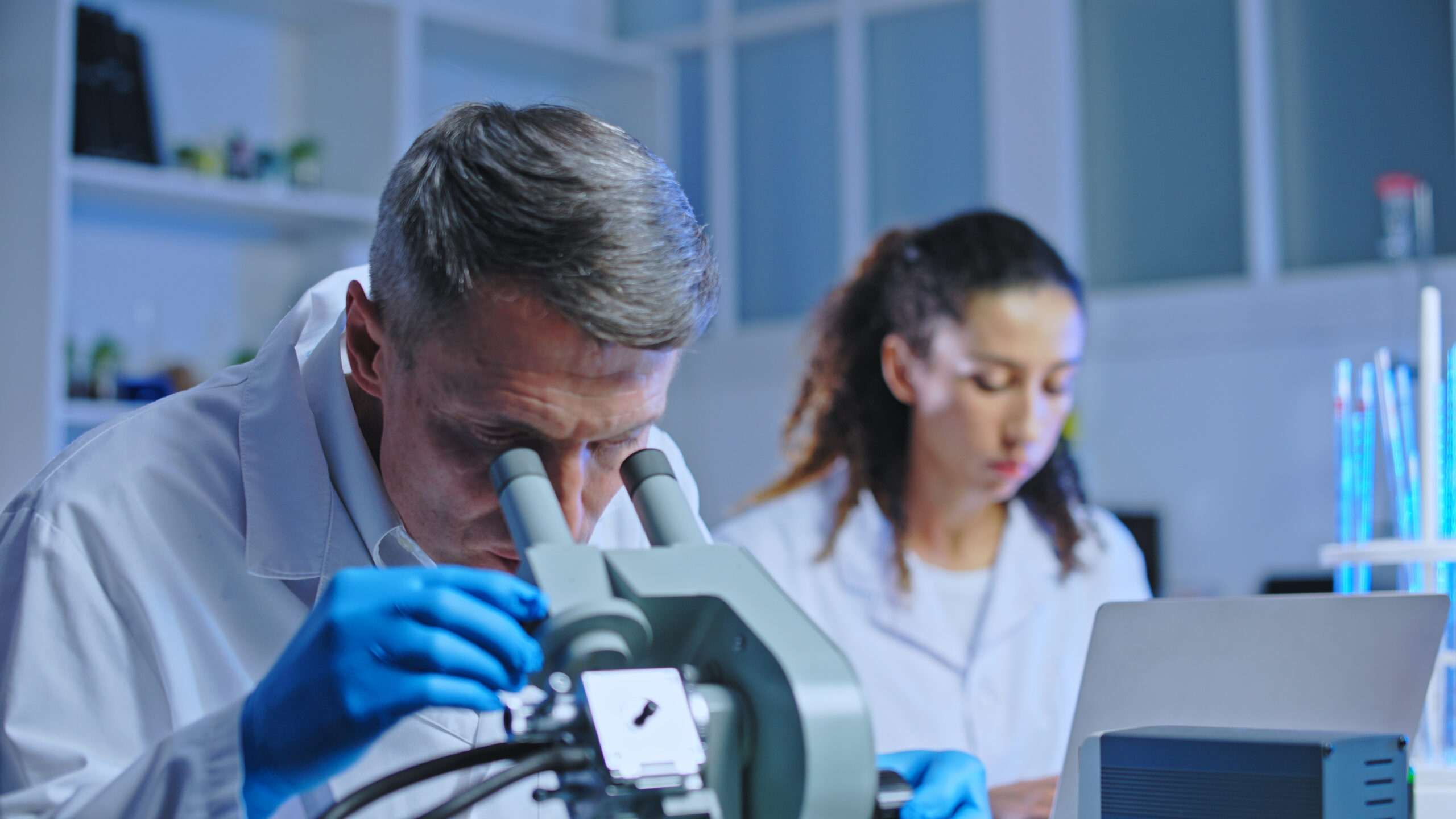 Oncology doctor examining tissue sample under microscope, clinical diagnostic lab